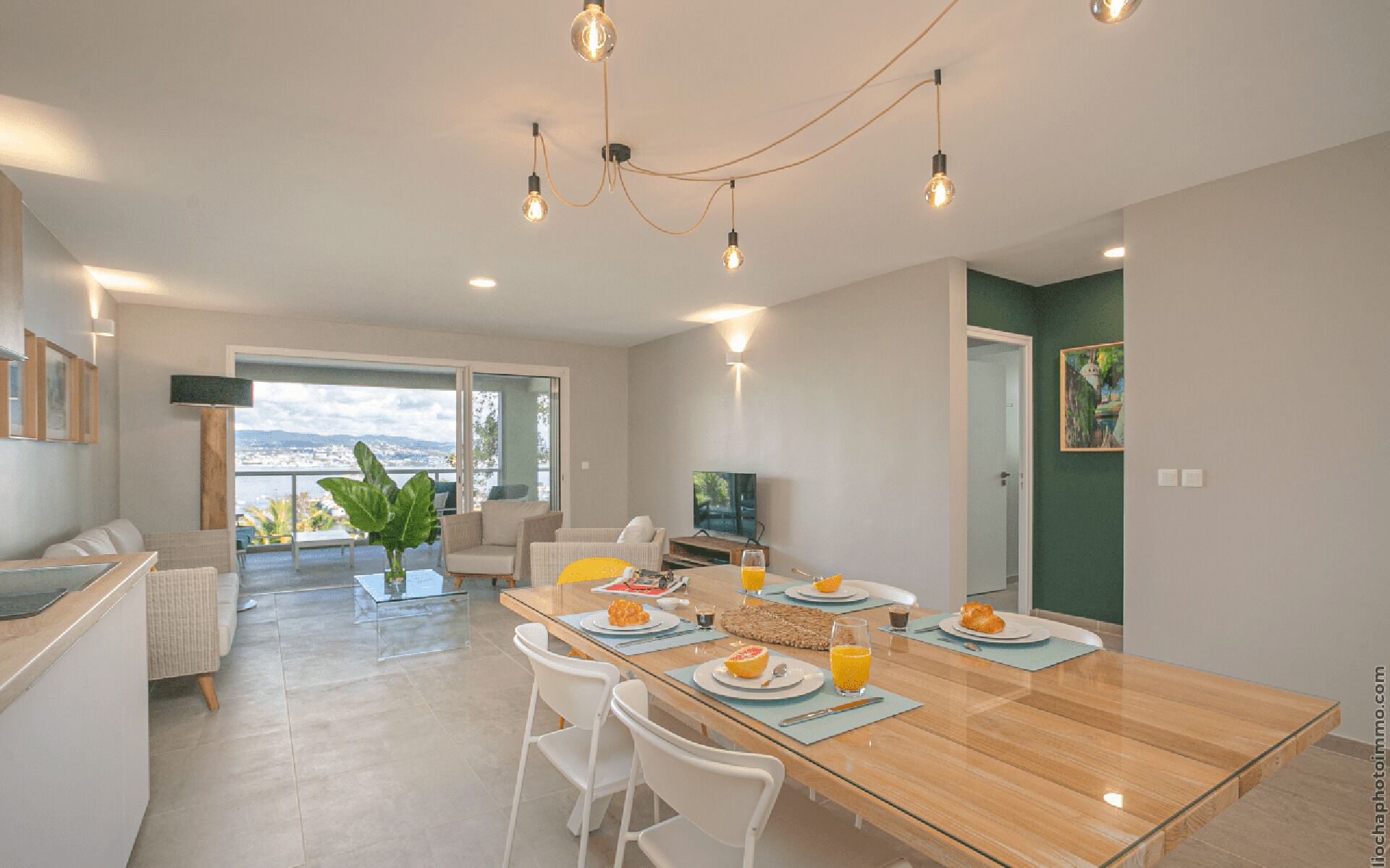 Un comedor moderno con una mesa de madera, sillas blancas y vistas de la ciudad a través de grandes ventanales.