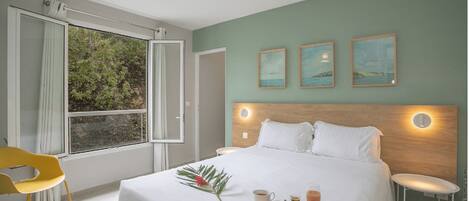 Une chambre d’hôtel avec un grand lit, une fenêtre avec des rideaux, une chaise jaune et un plateau de petit-déjeuner posé sur le lit.