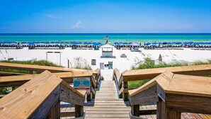 A wooden boardwalk leading to a beach with rows of blue umbrellas and lounge chairs. - Aqua 404 | Amazing Views, Incredible Amenities & Location! (Panama City Beach)
