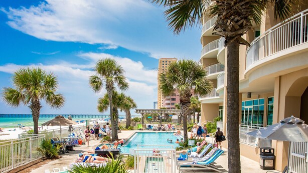 A pool area with lounge chairs and palm trees, overlooking a beach and ocean. - Aqua 404 | Amazing Views, Incredible Amenities & Location! (Panama City Beach)