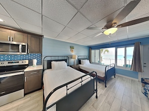 Une chambre d’hôtel avec une kitchenette, deux lits, un ventilateur de plafond et une vue sur l’océan.