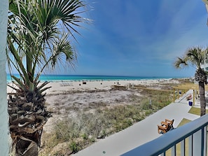 Une vue sur la plage depuis un balcon, avec un palmier, des chaises de plage et une terrasse en bois.