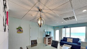 A room with a dining table, chairs, a sofa, a TV, and a view of the ocean. - Continental #320 | Gulf Front with Amenities! (Panama City Beach)