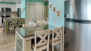 Een moderne keuken met een roestvrijstalen koelkast, een eettafel met glazen blad en witte kasten.