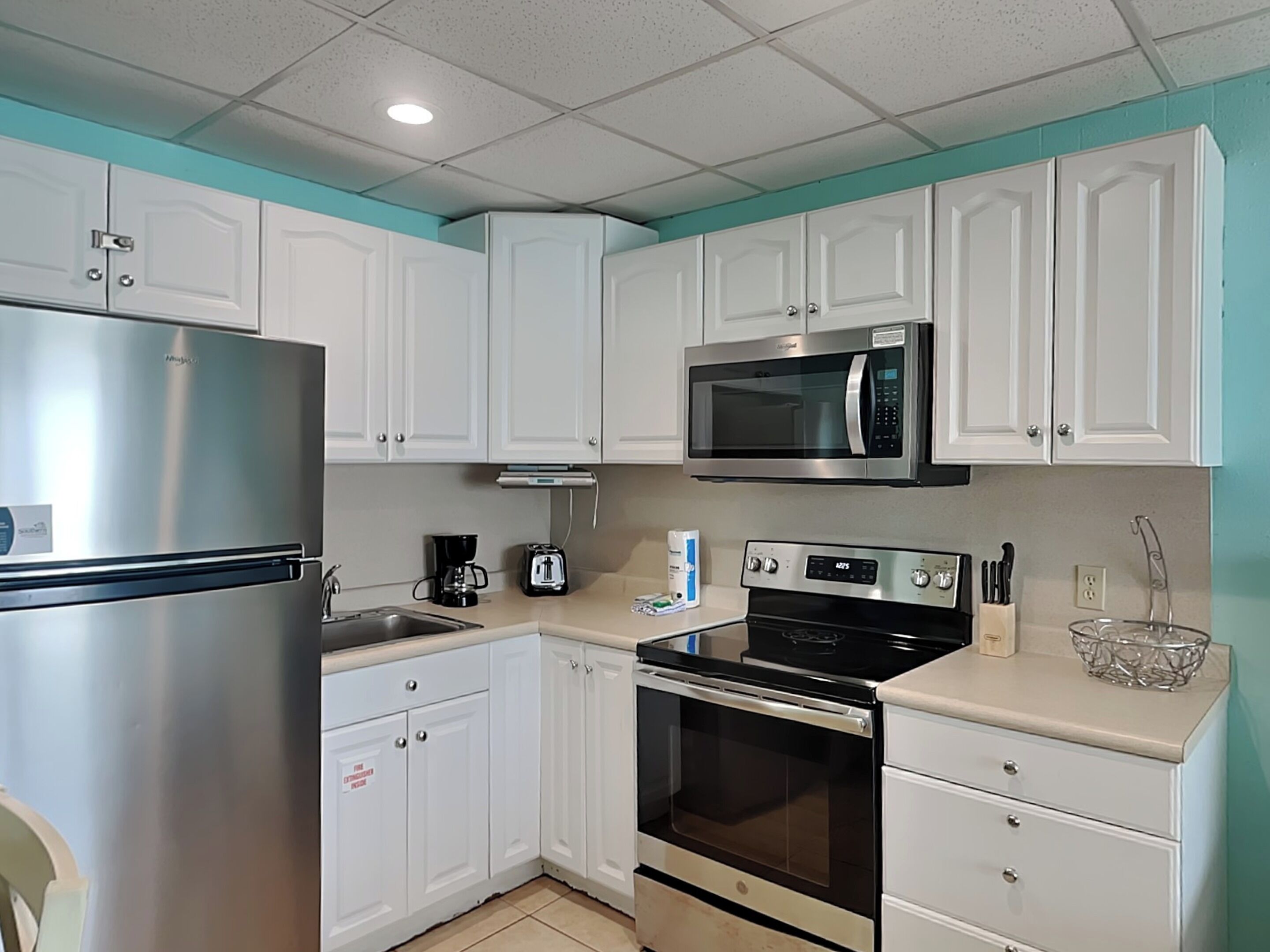 A modern kitchen with white cabinets, a stainless steel refrigerator, a microwave, a toaster, and an oven.