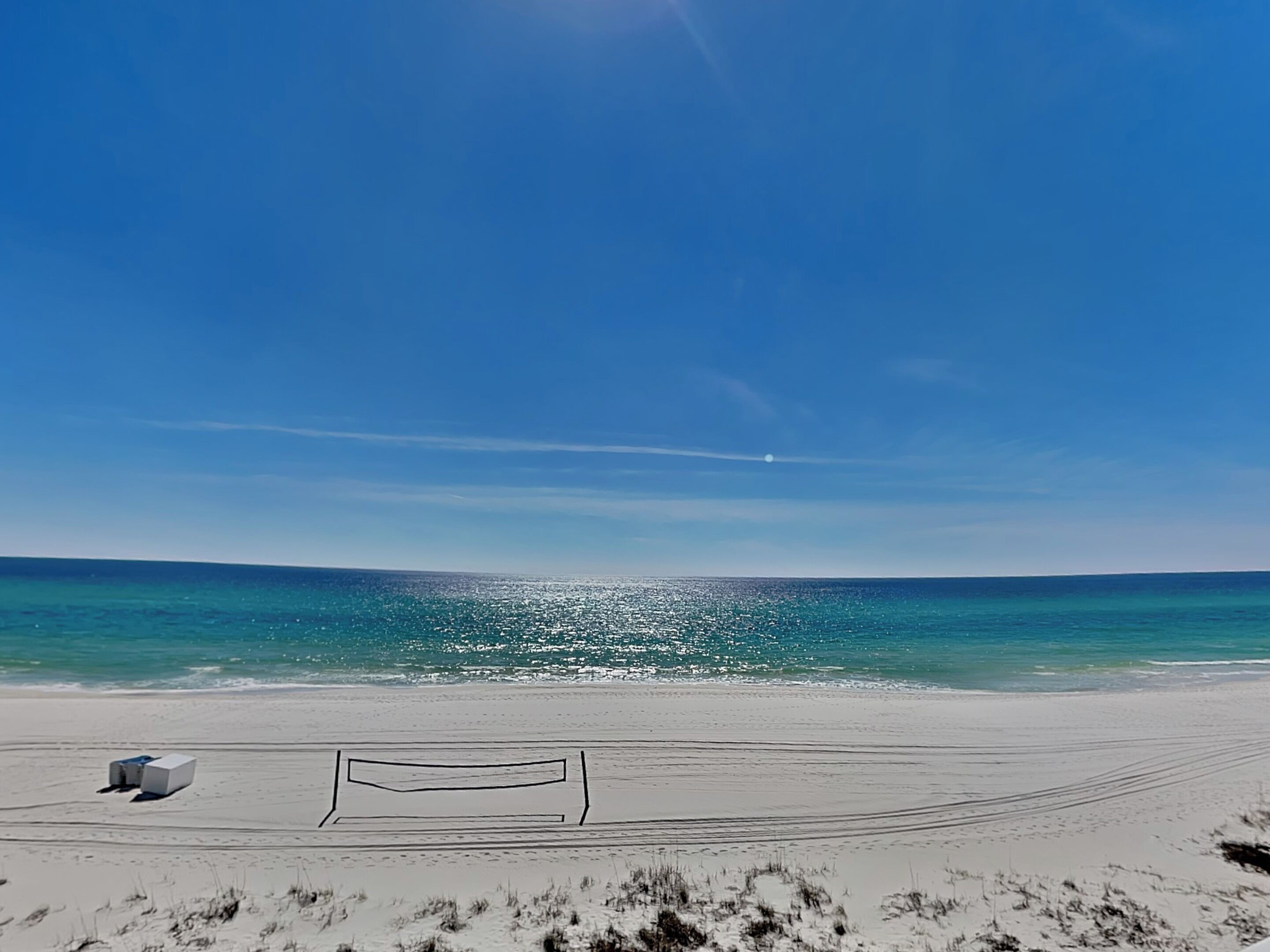 A beach with a volleyball net and a small white structure.