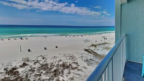 Vista a la playa desde un balcón, con cielo despejado, arena y mar.