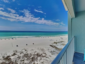 A beach view from a balcony with a clear sky, sandy beach, and ocean.
