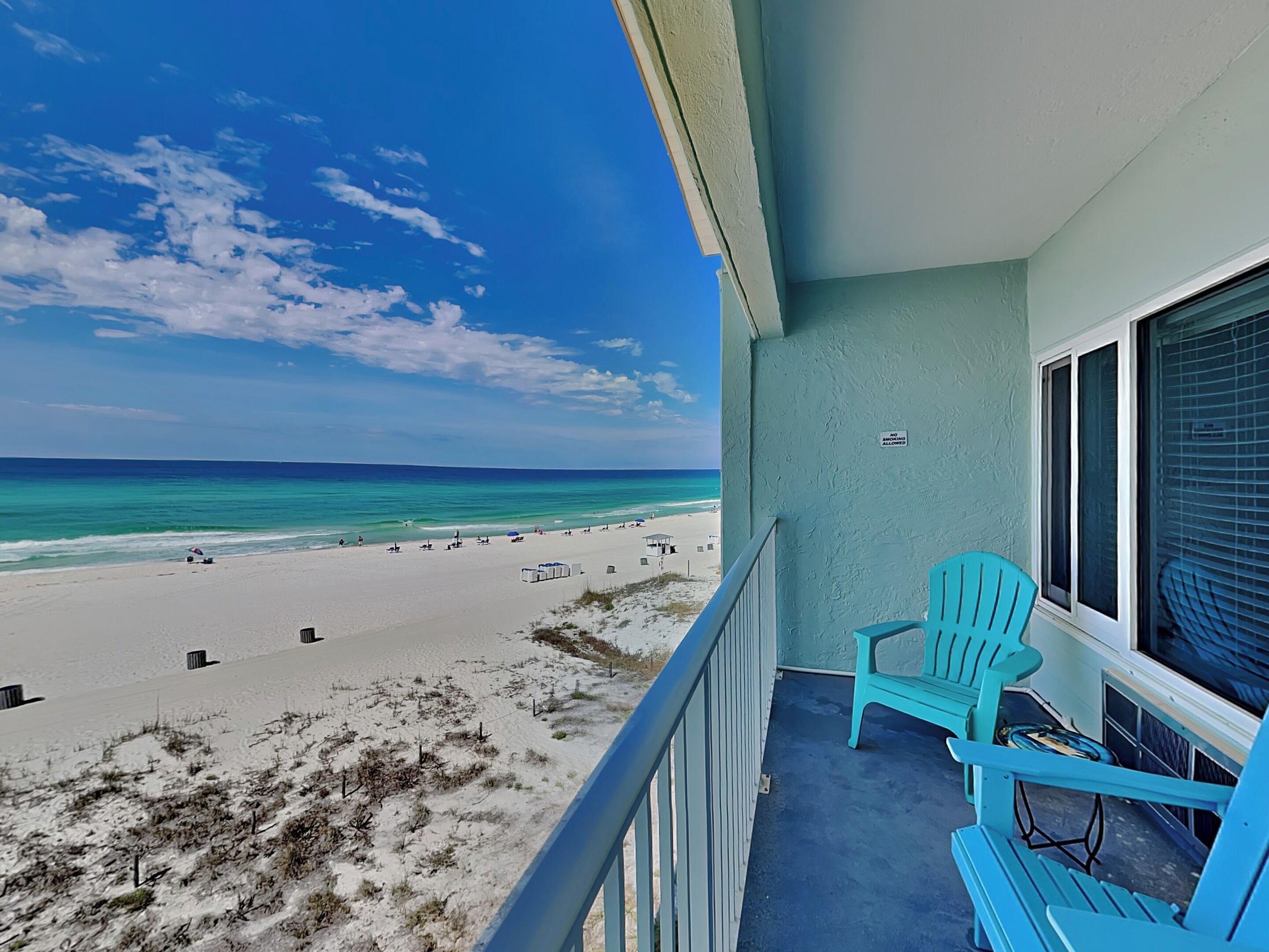 A balcony with a view of a beach, a sign indicating no smoking, and a turquoise chair.