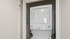 En hvid, kompakt vaskemaskine og tørretumbler-enhed med kontrolknapper og en startknap, installeret i et hjørne med en dør.