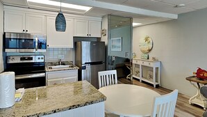 Een moderne keuken met witte kastjes, roestvrijstalen apparatuur, een granieten aanrecht en een eethoek met een witte tafel en stoelen.