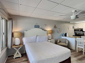 Ein Schlafzimmer mit einem großen Bett, Nachttischen mit Lampen, einem Sessel, einem Schreibtisch mit Stuhl und einer Küchenzeile.