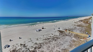 Blick auf einen Strand vom Balkon aus, mit blauem Himmel, Sandstrand und einem Pier in der Ferne.