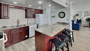 A modern kitchen with granite countertops, dark wooden cabinets, and a built-in island with bar stools. - Edgewater Leeward #306 | Gulf Front + Amenities (Panama City Beach)