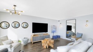 Uma sala de estar moderna com uma televisão de tela plana, uma mesa de centro de madeira e um espelho grande.