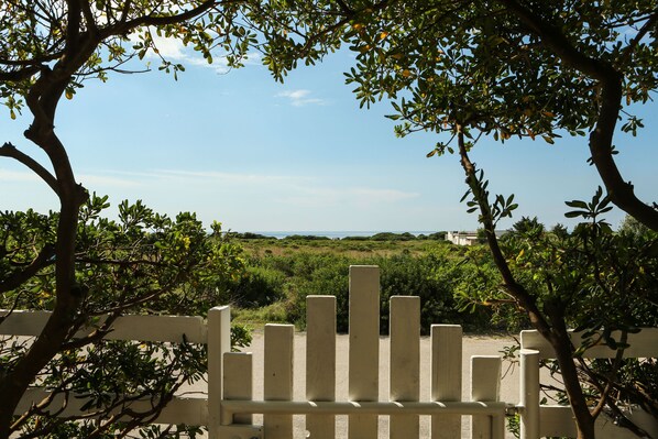 A white fence with vertical bars, surrounded by trees and shrubs, leading to a view of a distant landscape.