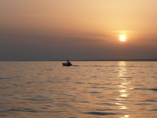 A sunset over a calm sea with a small boat in the distance. - At Teresa's House (Puglia)