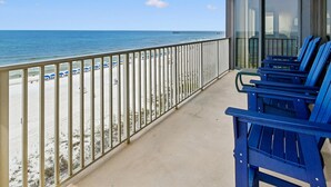 Un balcon avec vue sur la plage et l’océan, agrémenté de chaises bleues et d’une balustrade.