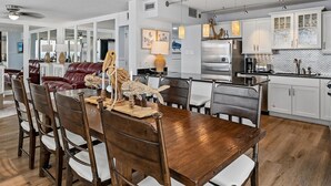 Une cuisine moderne avec des meubles blancs, un réfrigérateur en acier inoxydable et un coin repas comprenant des chaises et une table en bois.
