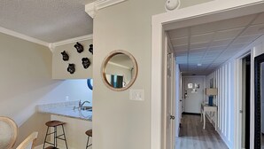 Een gang met een houten vloer, een spiegel en een deur naar een andere kamer.
