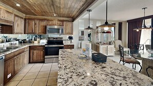 Una cocina moderna con armarios de madera, electrodomésticos de acero inoxidable, encimera de granito e iluminación colgante.