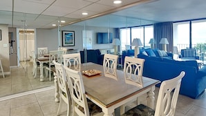 Una sala de estar moderna con un sofá azul, una mesa de comedor con sillas blancas y un ventanal con cortinas.