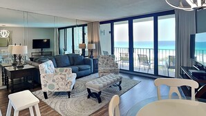 Un salón amplio con un gran ventanal con vistas al océano, un sofá cómodo, un comedor y un televisor.