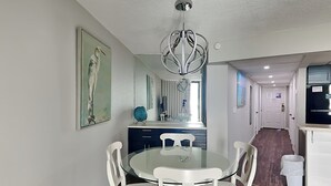 Una cocina moderna con armarios blancos, un refrigerador negro y un comedor con mesa de vidrio y sillas blancas.