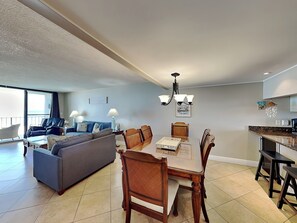 A modern living room with a gray sofa, dining table with chairs, and a kitchen area with a countertop and cabinets.
