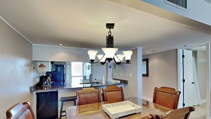 A modern kitchen with a central island, dining table with chairs, and a chandelier.