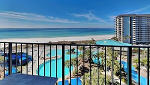 A view from a balcony overlooking a beach, a swimming pool, and a hotel building.