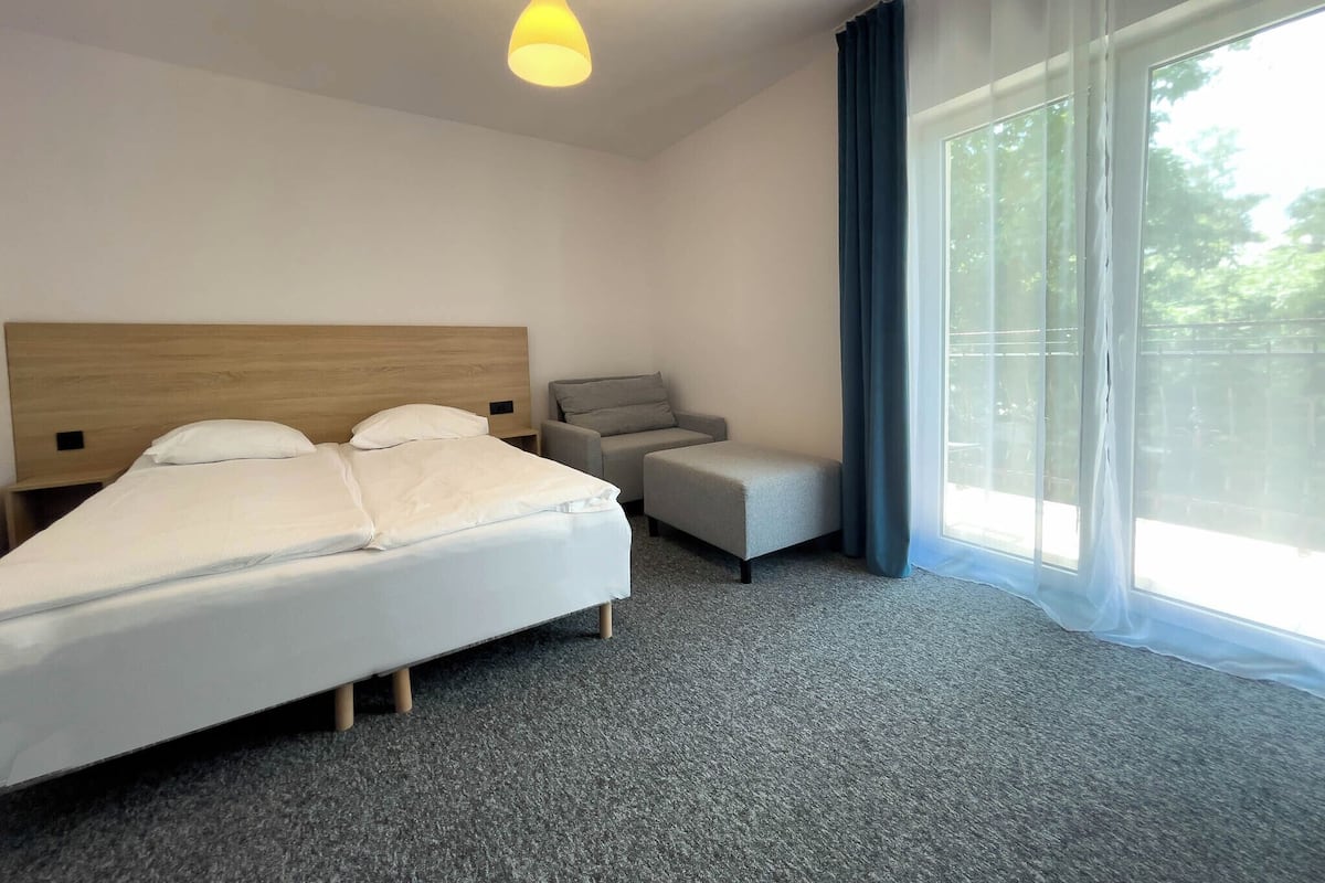 Ein Hotelzimmer mit einem Bett, einer kleinen Sitzecke, einem Nachttisch und einem großen Fenster mit Vorhängen.