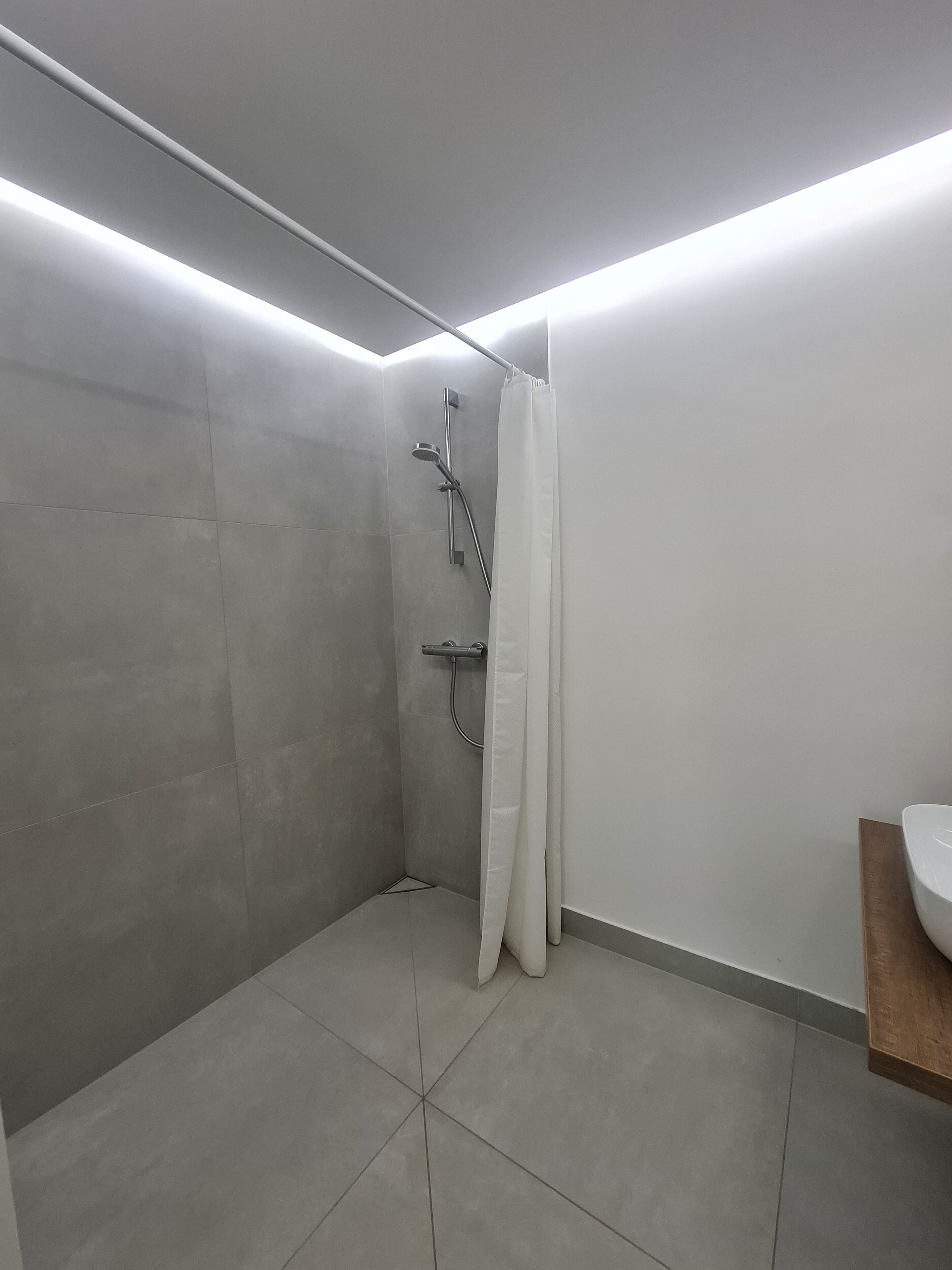 A modern bathroom with a shower, a white sink, and a wooden countertop.