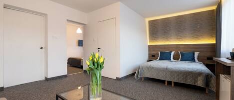A modern hotel room with a bed, bedside table, and a glass coffee table with a vase of flowers.