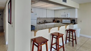 Une cuisine avec des meubles blancs, un plan de travail en granit, une cuisinière, un four à micro-ondes et trois tabourets en bois.