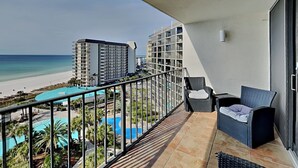 Ein Balkon mit Blick auf Strand und Pool. Zwei Korbstühle und ein kleiner Tisch sind vorhanden.