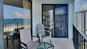 Un balcón con vista al océano, una silla, una mesa y un ventanal corredero.