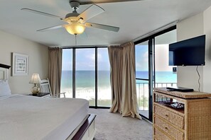 Une chambre d’hôtel équipée d’un lit, d’un ventilateur de plafond, d’une télévision, d’une commode en osier et d’un balcon avec vue sur l’océan.