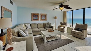 A spacious living room with a large window offering a view of the ocean, a ceiling fan, and a modern interior design.