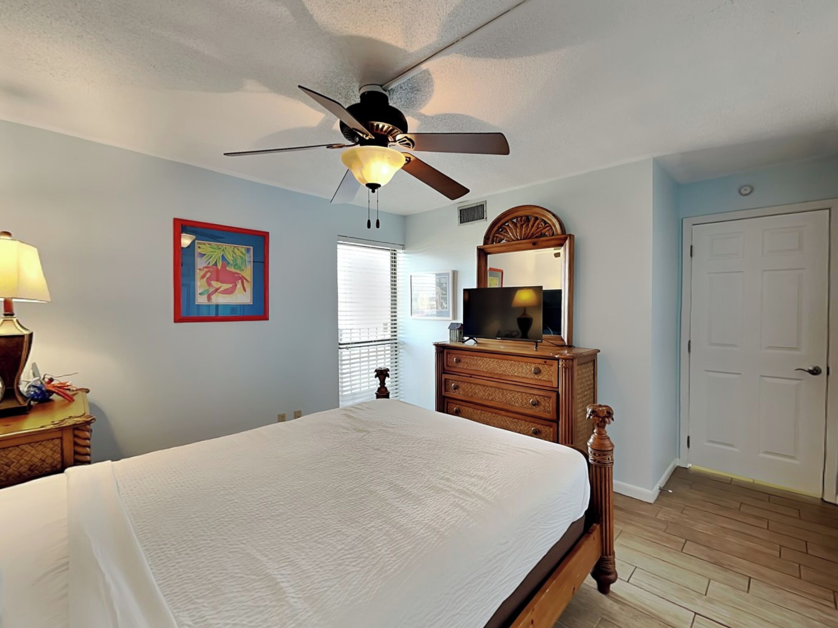 Une chambre à coucher avec un lit, un ventilateur de plafond, une commode, un téléviseur et une porte.