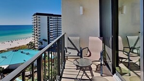 A balcony with a view of the beach and ocean, a pool, and outdoor furniture.