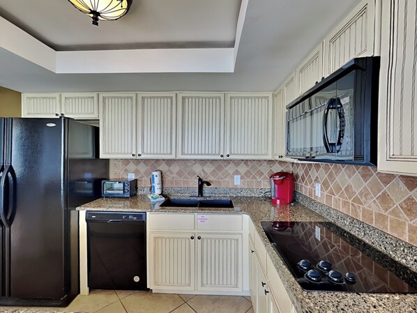 A modern kitchen with white cabinetry, a black refrigerator, a dishwasher, a microwave, and a gas stove.