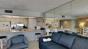 Un salon moderne comprenant un canapé, deux fauteuils, une table basse et un coin cuisine équipé d’un réfrigérateur, d’un four à micro-ondes et d’une cuisinière.