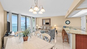 Una sala de estar moderna con comedor, una cocina con barra y grandes ventanales con vista al océano.