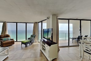 A balcony with a TV, seating, and a view of the ocean.
