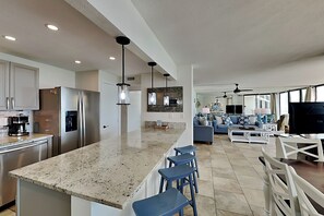 A modern kitchen with a granite countertop, stainless steel appliances, and a bar area with stools.