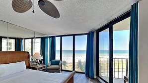 Habitación de hotel con una cama grande, una silla, una mesita de noche y vista a la playa.