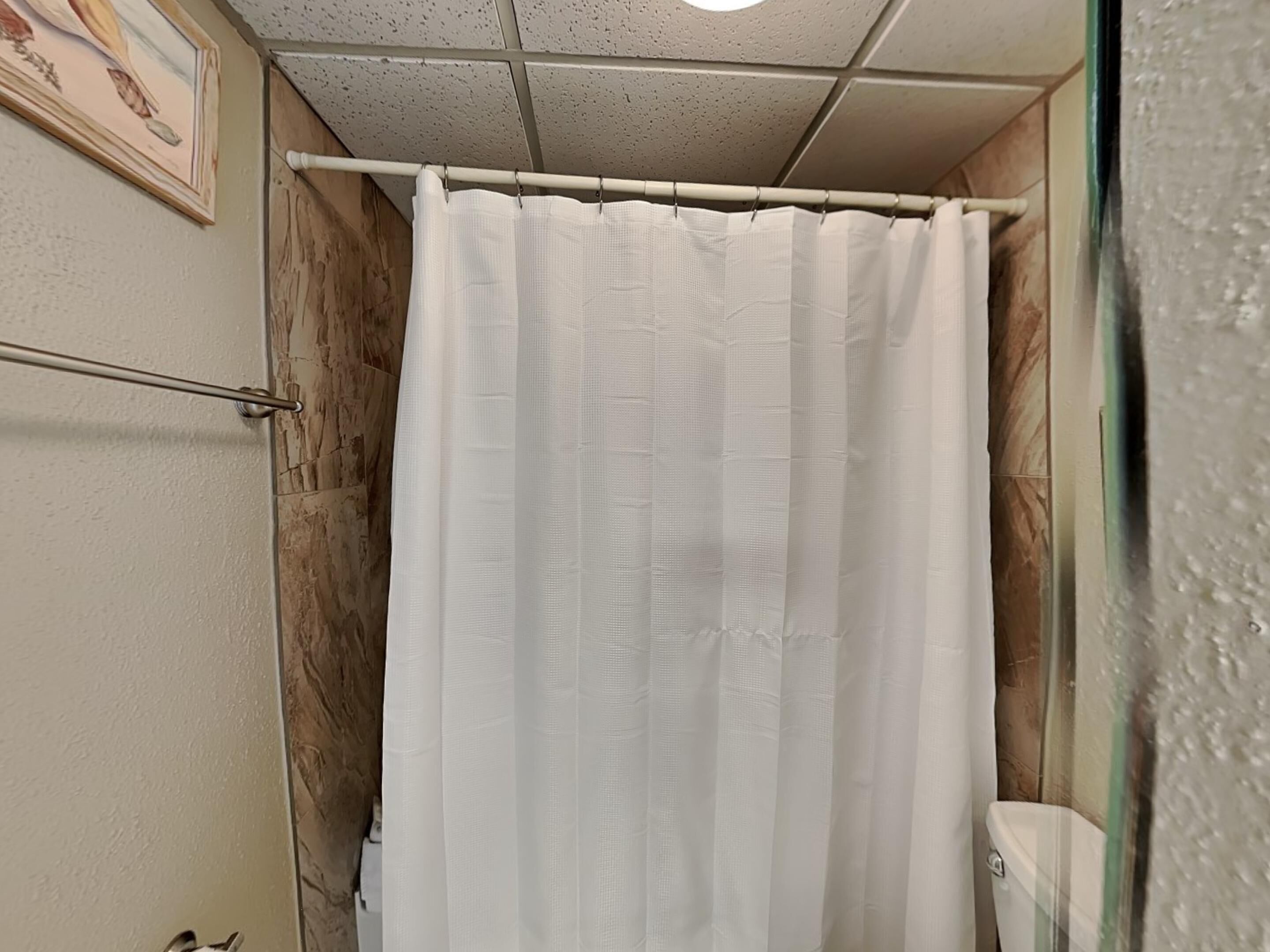 A bathroom with a white shower curtain, a wooden wall, and a toilet.