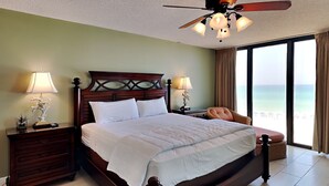 A spacious bedroom with a large bed, two bedside tables with lamps, a ceiling fan, and a view of the beach. - Edgewater Tower II #303 | Balcony Views + Resort Amenities! (Panama City Beach)