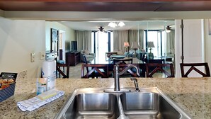 A kitchen with a double sink, wooden cabinets, and a dining area visible through a large mirror. - Edgewater Tower II #303 | Balcony Views + Resort Amenities! (Panama City Beach)